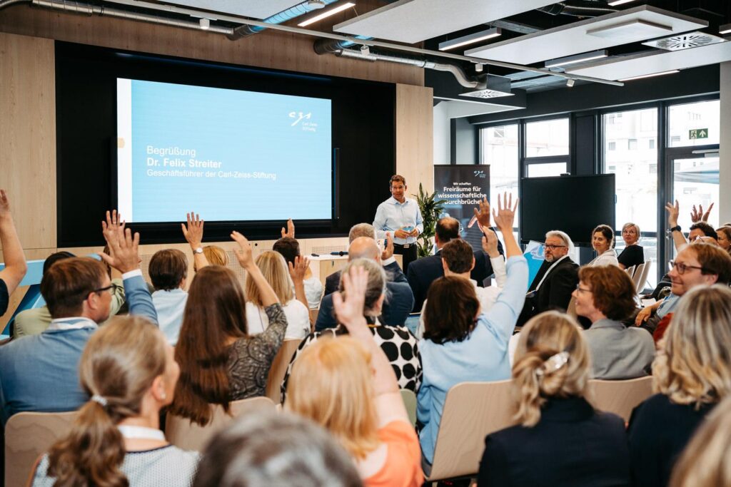 Eventfotograf Kaiserslautern – interaktiver Vortrag bei einem Corporate Event: Speaker vor Leinwand, Publikum hebt die Hände